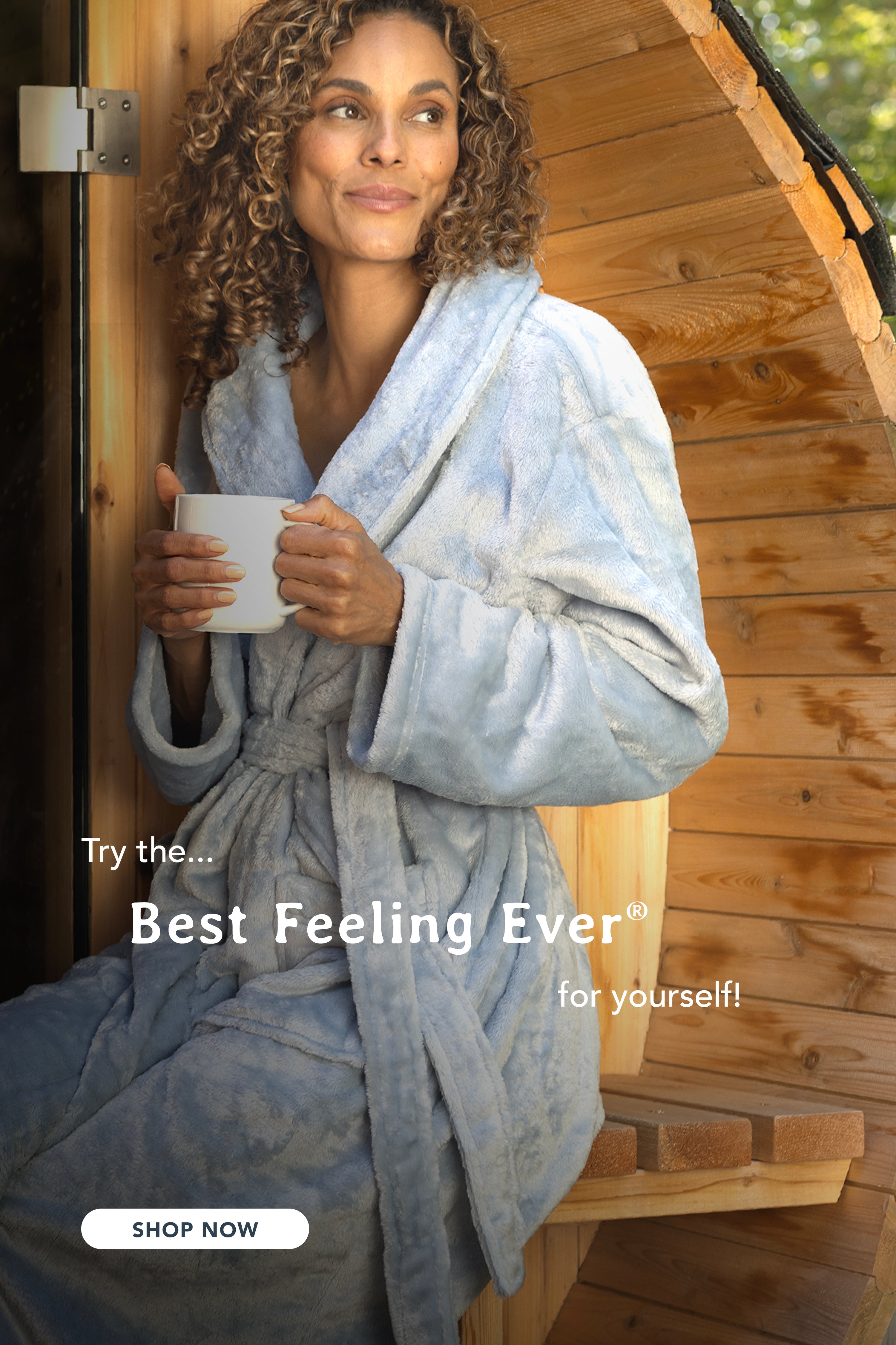 A woman holding a mug while standing outside fo a sauna in a VelvetLoft Robe with the message "Feel the best feeling ever for yourself!".
