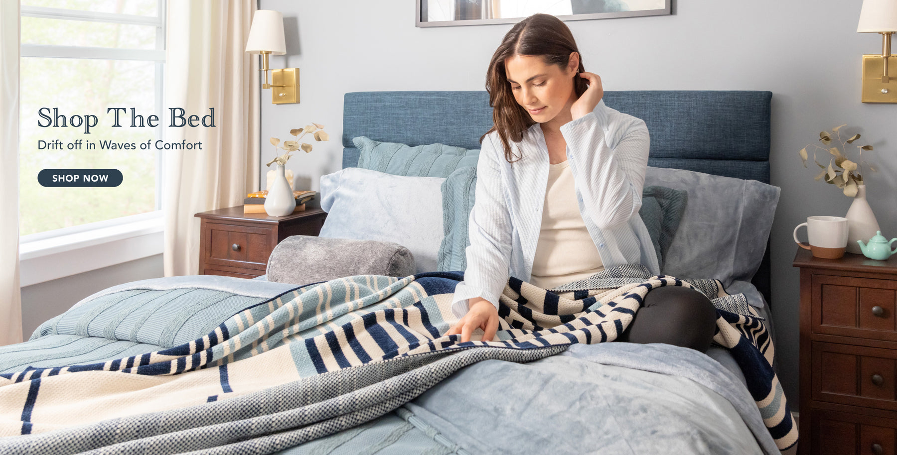 Shop the bed. Drift off in waves of comfort. Shop now. Image of woman sitting in bed styled with blue and striped products.