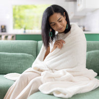 Person sitting on a couch, gently holding the White Retro Comfort Plush throw, creating a cozy, relaxed scene.