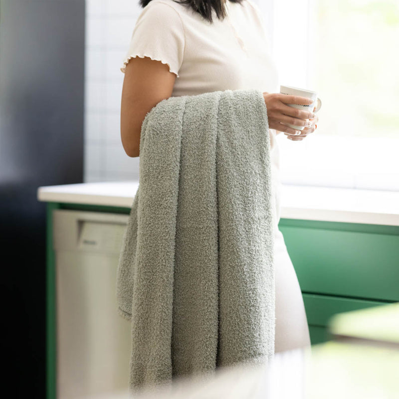 Person holding a mug and the Farmhouse Sage throw is draped over her arm demonstrating its soft and thick fabric