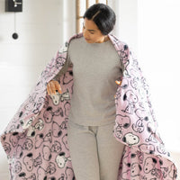 Woman holding a pink blanket with cartoon characters, wearing a gray outfit.