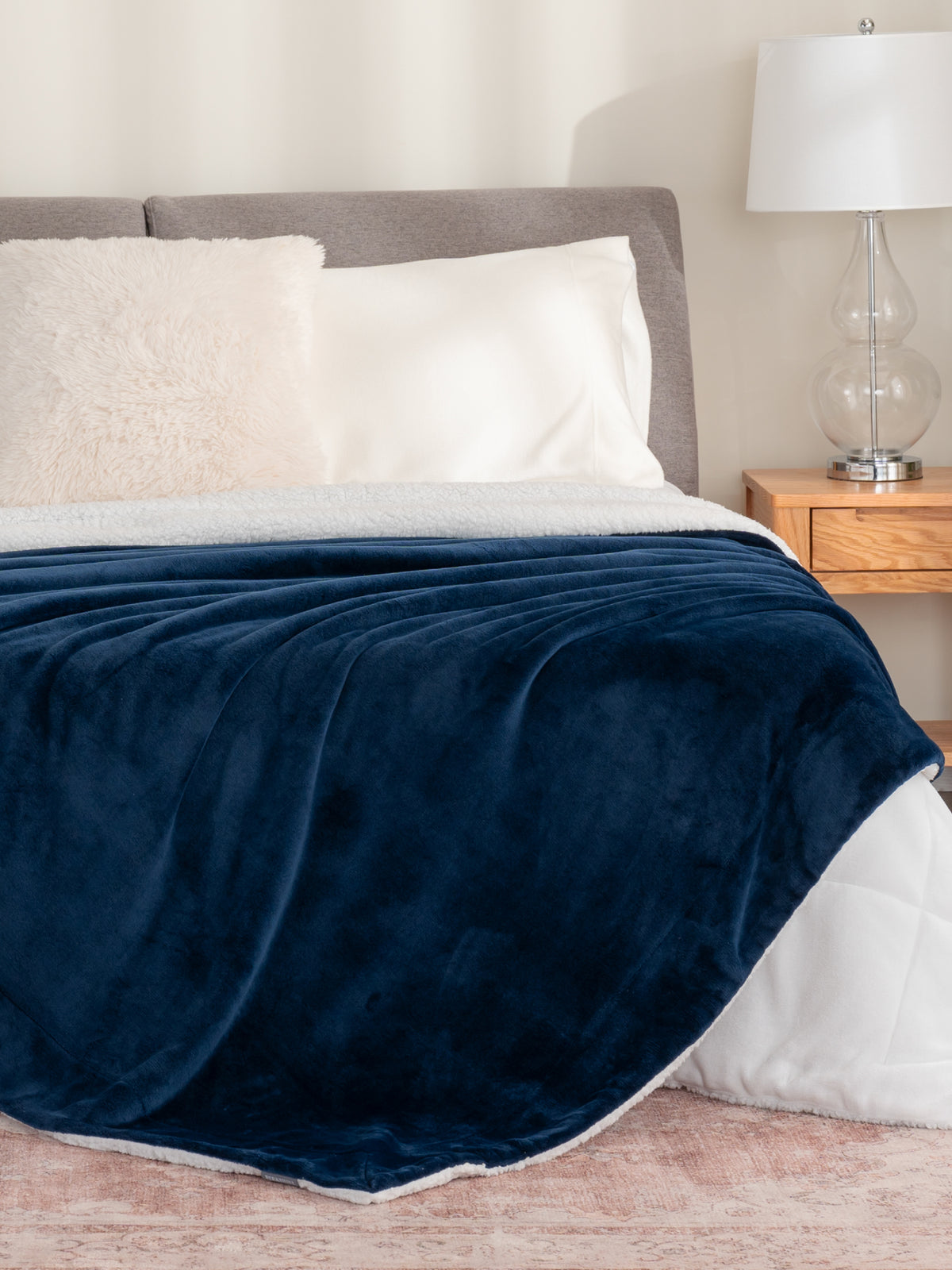 Blankets collection image featuring our VelvetLoft Sherpa Blanket in navy draped over a white bed.