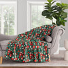 Christmas-themed blanket draped over a gray sofa in a room with large windows and a plant.