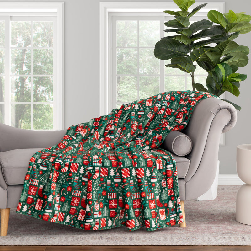 Christmas-themed blanket draped over a gray sofa in a room with large windows and a plant.