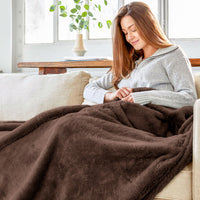 A woman sitting on a couch with a brown throw over her legs.