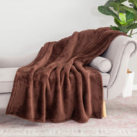 A brown Extra-Fluffy Throw draped over the arm of a beige chair in a bright room with a plant behind it.