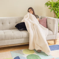 A woman wrapped up in a cream colored throw blanket.