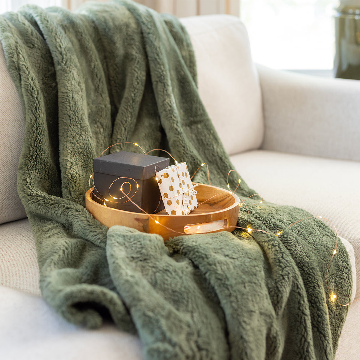 Green blanket draped over a couch with a wooden tray holding a gift and polka dot container.