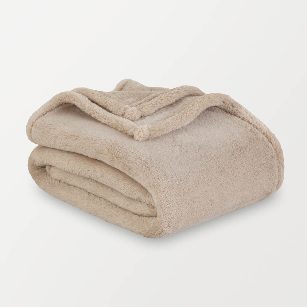 A tan extra-fluffy throw folded enatly on a white surface.