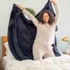 Woman in pajamas holding a dark blue blanket in a bedroom