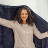Woman holding a navy blue blanket above her head with a white background