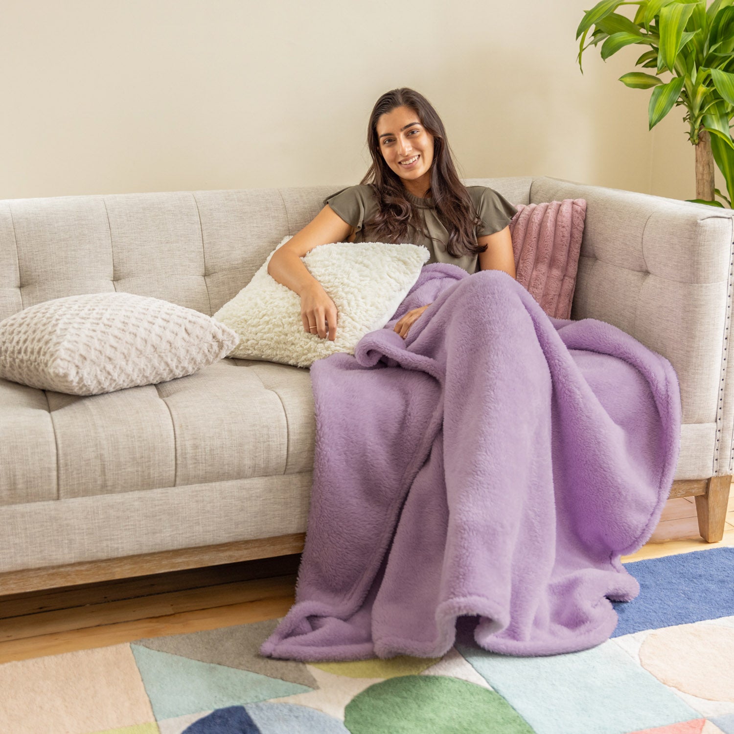 A woman sitting on a sofa with a purple throw blanket.