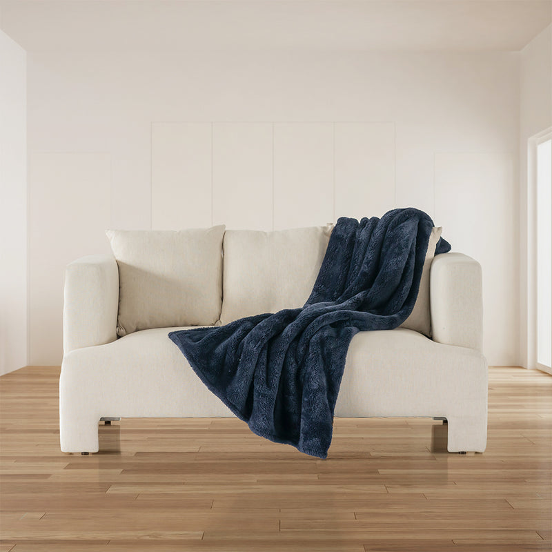 A navy blue Extra-Fluffy Throw draped over a white couch in a bright, minimalist room.