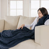 A woman lounging on a white sofa, wrapped in a navy blue Extra-Fluffy Throw.