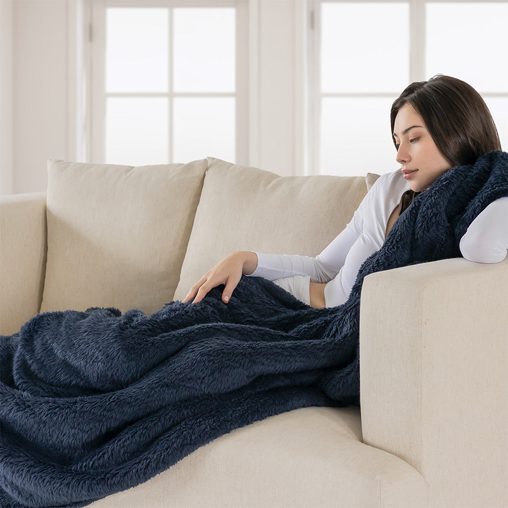 Image of a woman on a couch with a blue Extra-Fluffy™ Throw