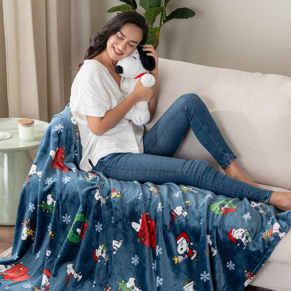 Woman sitting on a couch with a Snoopy-themed blanket and plush toy
