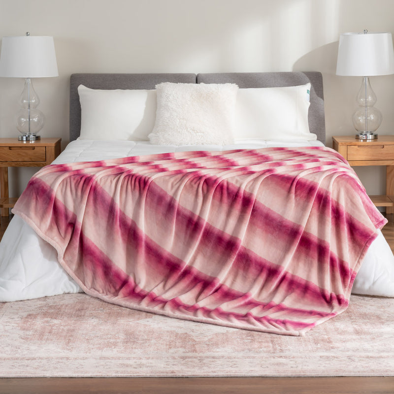 Pink ombre velvety plush bed blanket draped neatly on a white bed in a bedroom setting.