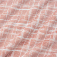 Close up peach colored plaid velvety plush bed blanket displaying its silky smooth texture.