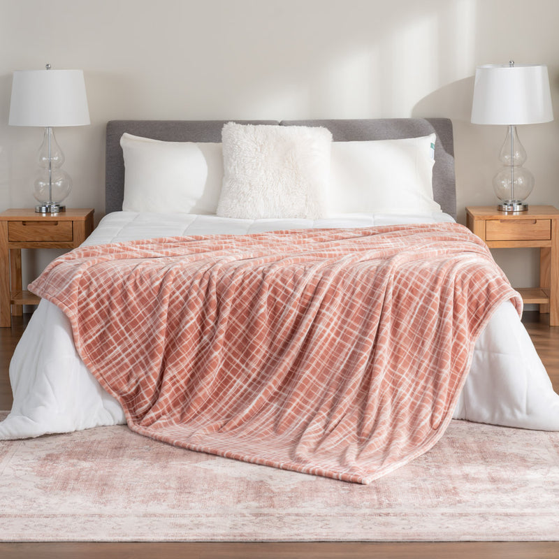 Peach colored plaid velvety plush bed blanket draped neatly on a white bed in a bedroom setting.