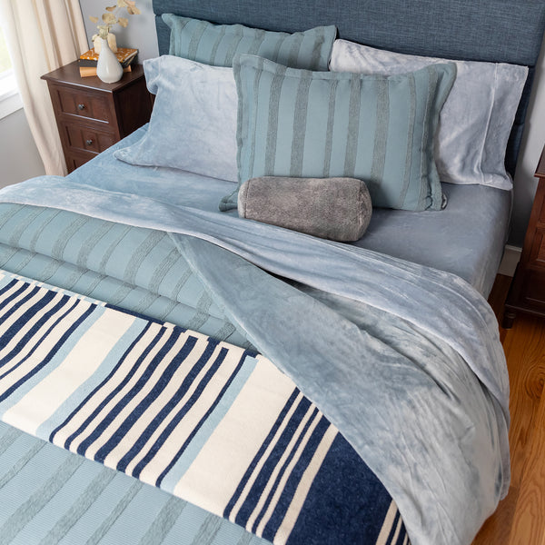 A blue decorated bed dressed with light blue velvety sheets in a bedroom.