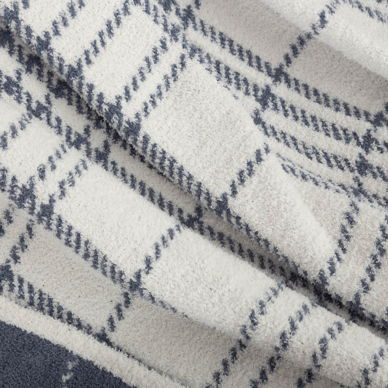 A close up of a white and blue plaid knitted throw, displaying its soft and strechy texture.