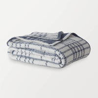 A white and blue plaid knitted throw folded neatly on a white surface.