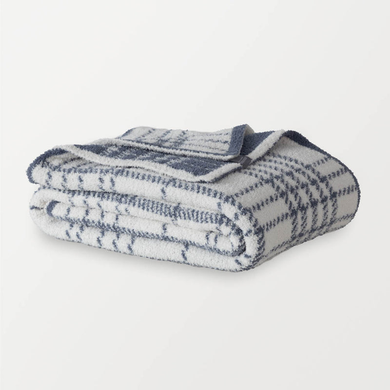 A white and blue plaid knitted throw folded neatly on a white surface.