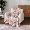 Patterned blanket draped over a beige armchair in a room with wooden furniture and a plant.