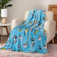 Blue cartoon-themed blanket draped over a chair in a room with a lamp and plant.