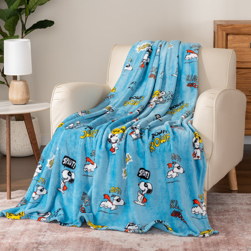 Blue cartoon-themed blanket draped over a chair in a room with a lamp and plant.
