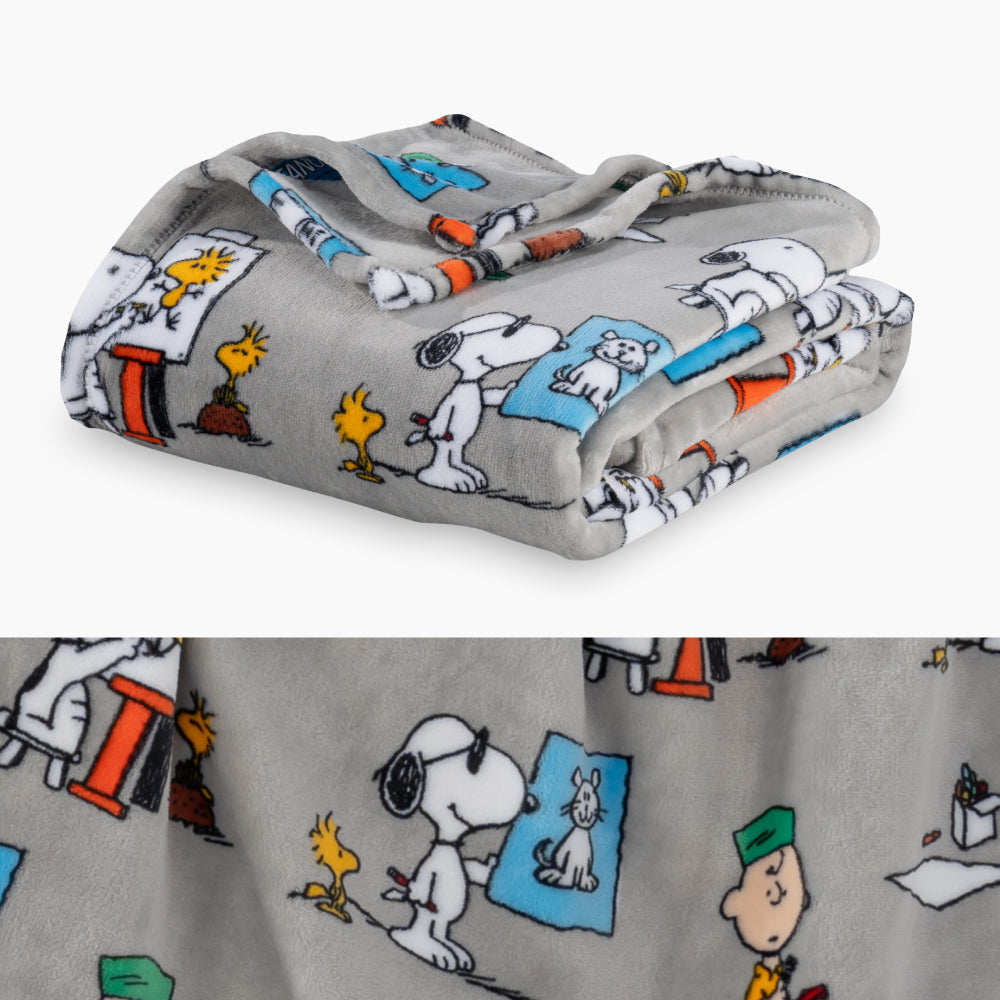 A grey peanuts art class throw folded neatly on a white surface with a close up image underneath.