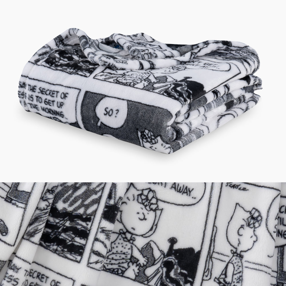 Black and white printed comic peanuts throw folded nearly on a white surface with a close up image underneath.