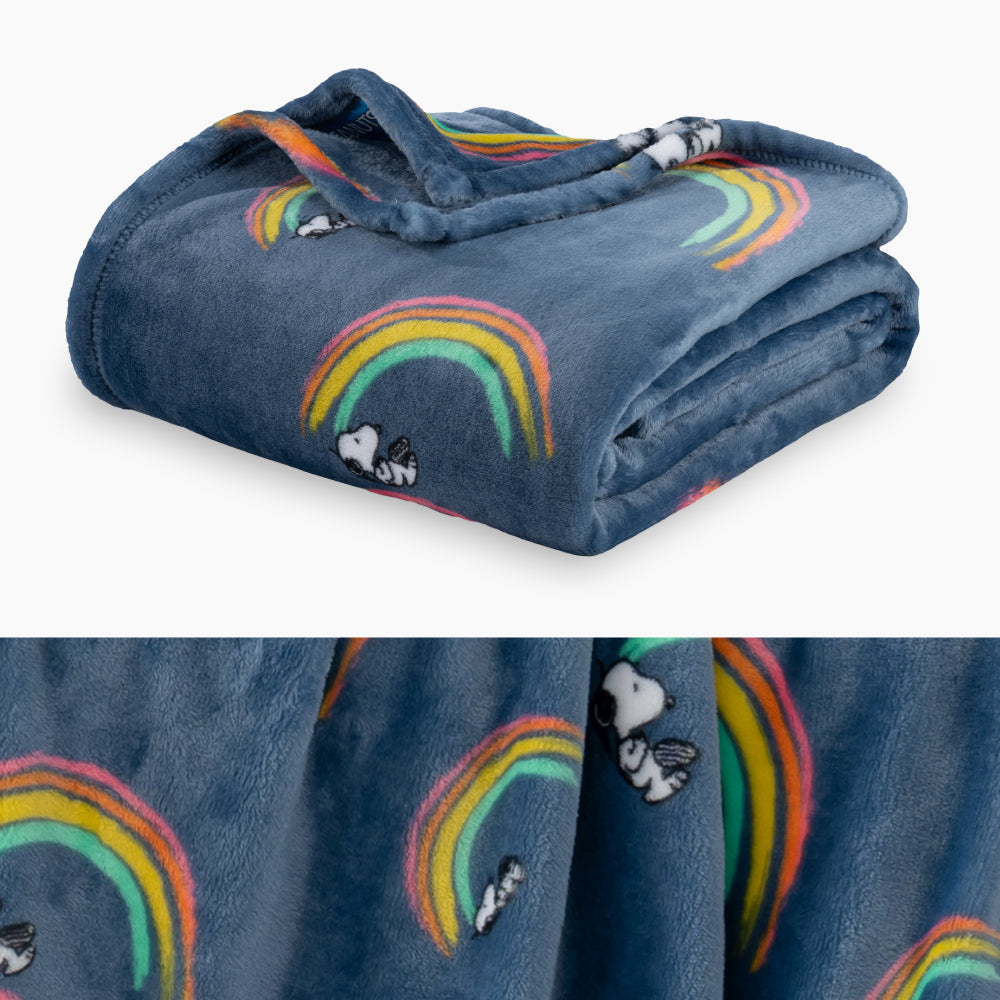 A blue rainbow snoopy throw folded neatly on a white surface with a close up image underneath.