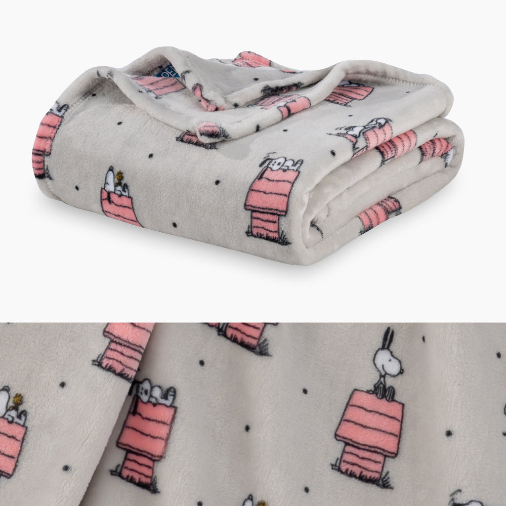 A grey and pink polka dot snoopy throw folded neatly on a white surface with a close up image underneath.