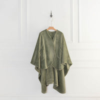 An olive green PrimaLush Cape Wrap draped on a hanger against a white wall.