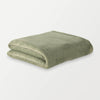 A folded olive green PrimaLush Cape Wrap resting on a white surface.