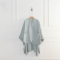 A light blue PrimaLush Cape Wrap hanging neatly on a wall hook against a white background.