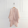 A blush pink PrimaLush Cape Wrap draped on a hanger, displayed in a bright space.