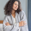 Woman wrapped in a gray cape wrap, standing indoors with a neutral background