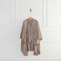 A taupe PrimaLush Cape Wrap hanging neatly on a wall hook against a white wall.