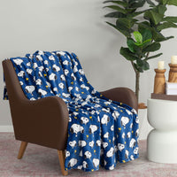 Cobalt blue printed Peanuts Throw draped neatly over a brown leather chair next to a side table and plant.