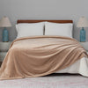 An almond seed colored velvet blanket draped over a bed with white pillows and blue lamps.