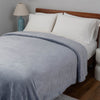 A light blue velvet blanket draped over a bed with white pillows and blue lamps.