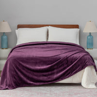 A plum velvet blanket draped over a bed with white pillows and blue lamps.