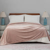 A light pink velvet blanket draped over a bed with white pillows and blue lamps.