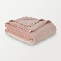 A folded light pink velvet blanket displayed on a white surface.