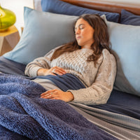 A woman laying in a bed decoratedwith blue bedding.