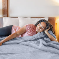 A woman laying on a bed with a fluffy blue blanket.