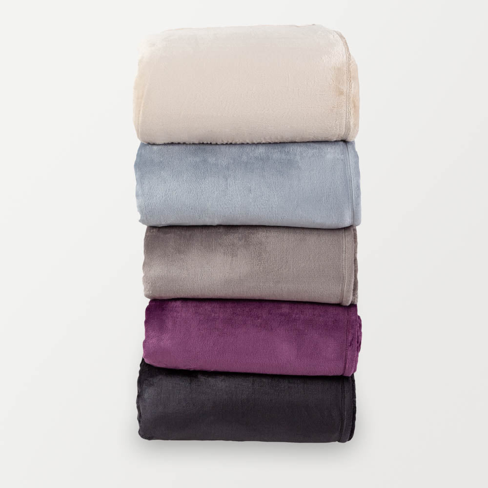 Stack of 5 velvety plush family blankets in cream, blue, grey, purple and black folded neatly on a white surface.