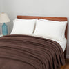 Polartec blanket in brown draped over a bed, paired with white pillows and a blue lamp on the side.